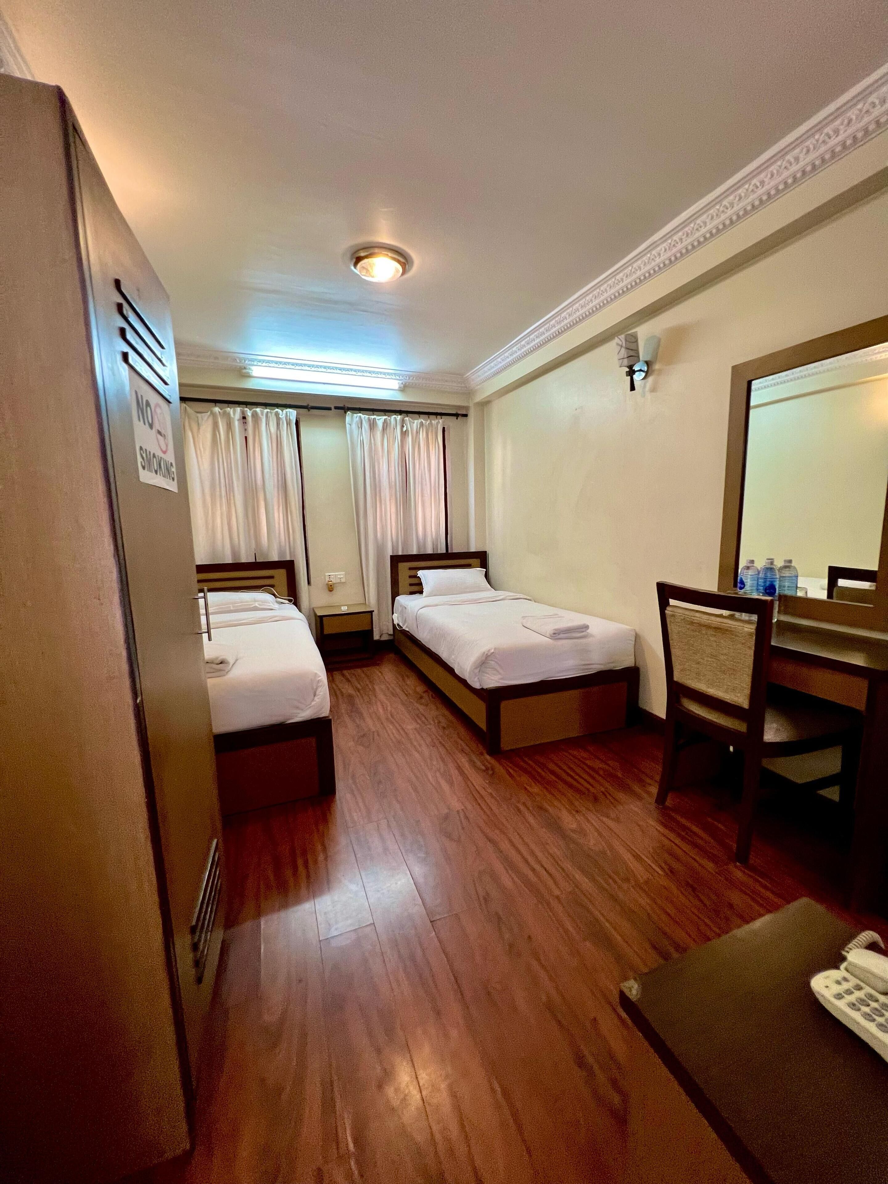 A hotel room with two single beds, a wooden floor, a desk with a telephone, and a mirror.