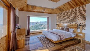 A modern bedroom with a large bed, wooden flooring, a view of the outdoors, and a brick-patterned wall. - The Tahoma Stays (Dhari)