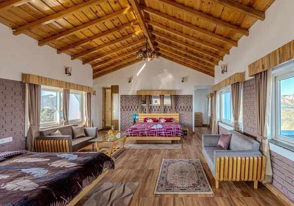 A spacious bedroom with a high wooden ceiling, a large bed, a sofa, and a view of the outdoors through the windows.