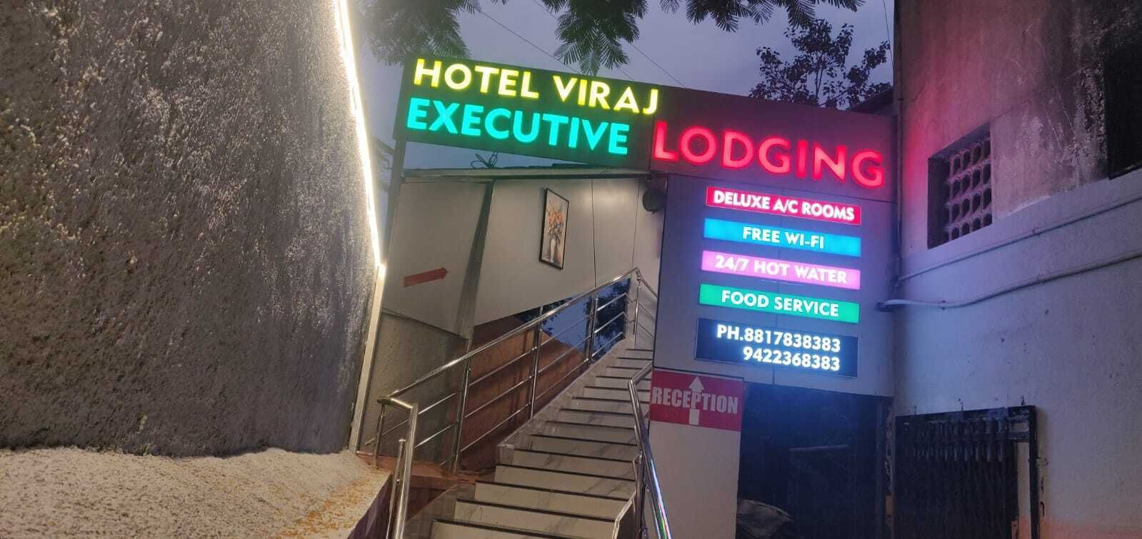 A hotel entrance with a neon sign advertising 'Hotel Viraj Executive Lodging'.