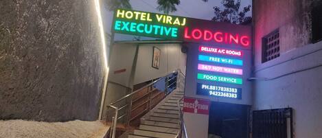 A hotel entrance with a neon sign advertising 'Hotel Viraj Executive Lodging'.