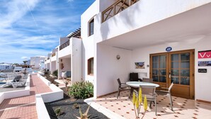 Edificio residencial con patio que incluye una mesa, sillas, un pequeño jardín y vista al mar.
