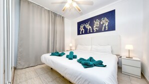 Habitación de hotel con una cama grande, un ventilador de techo, un cuadro de astronautas y una mesita de noche con lámpara.