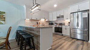 Una cocina moderna con armarios blancos, electrodomésticos de acero inoxidable y una isla central con taburetes de bar.