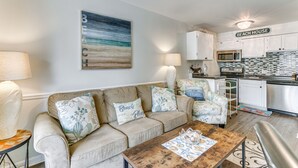 A living room with a beige sofa, a coffee table, and a painting of a beach scene. - Hilton Head Island Condo w/ Coligny Beach Access! (Hilton Head Island)