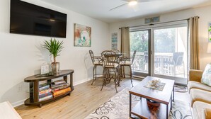 A modern living room with a flat-screen TV, a dining table with chairs, a ceiling fan, and a large window with a view of the outdoors. - Hilton Head Island Condo w/ Coligny Beach Access! (Hilton Head Island)