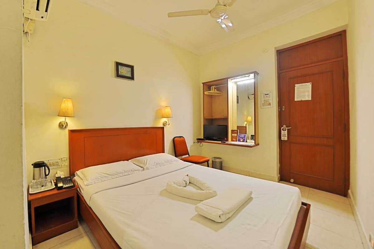 Habitación de hotel con cama, lámparas de noche, escritorio con computadora, silla, televisor y puerta.