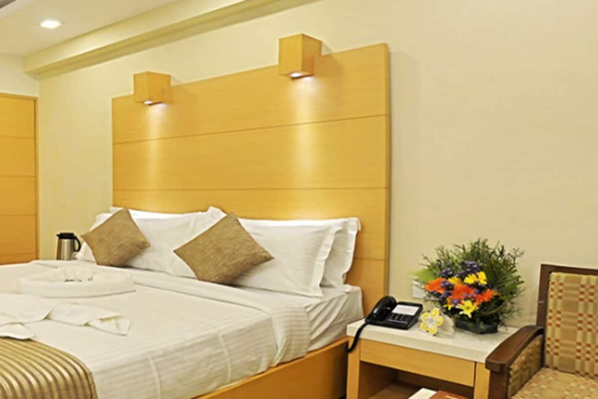 Habitación de hotel con cama, mesita de noche, silla y un pequeño escritorio con teléfono.