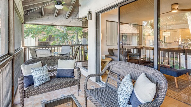 A covered outdoor seating area with wicker furniture and a glass door leading to an interior space. - Condo in PGA National Resort w/ Pool & Spa! (Palm Beach Gardens)