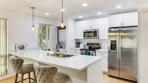 A modern kitchen with a central island, stainless steel appliances, and pendant lighting. - Condo in PGA National Resort w/ Pool & Spa! (Palm Beach Gardens)