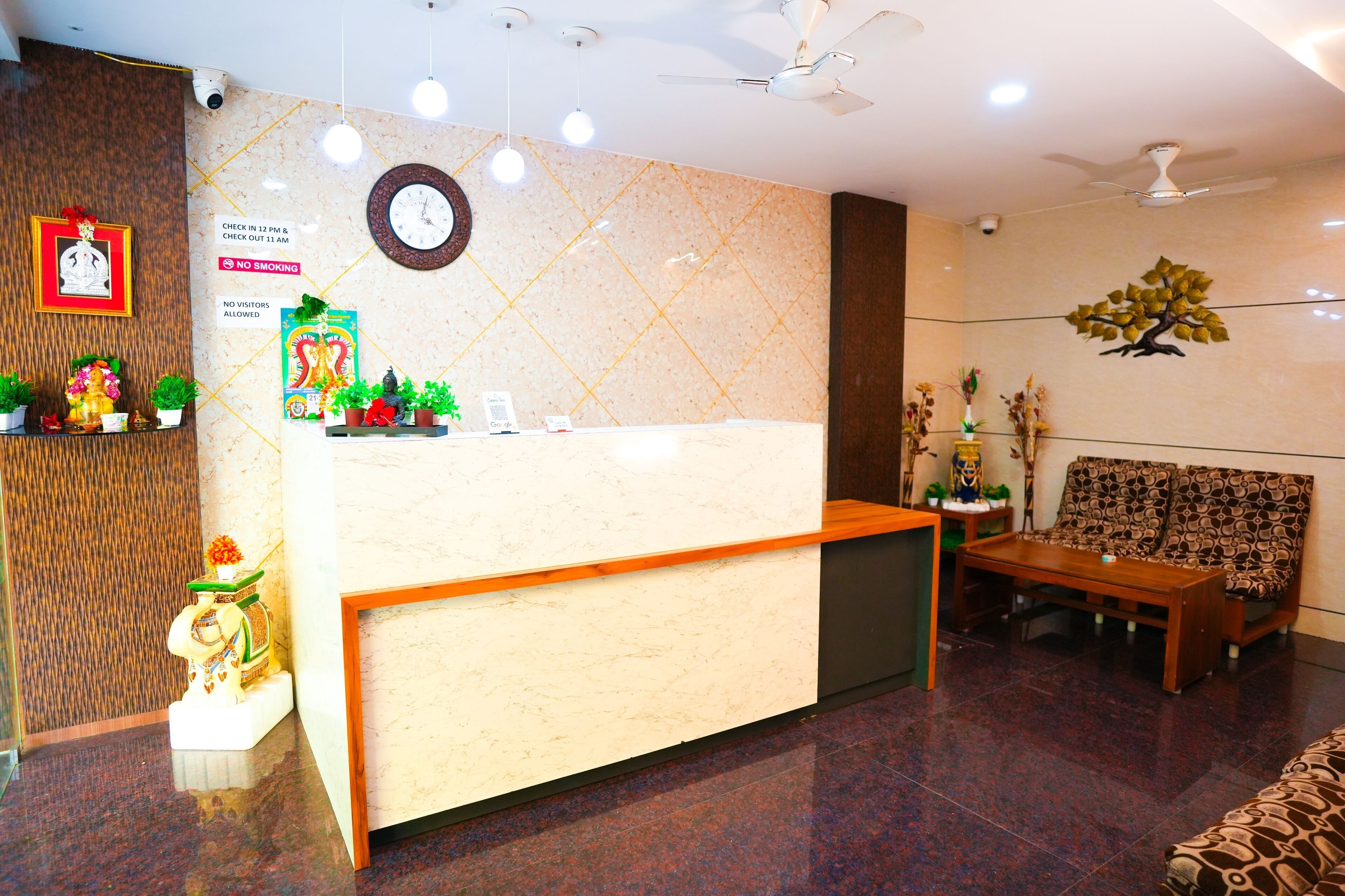 A hotel reception area with a marble wall, a reception desk, a clock, and a seating area with a patterned sofa.