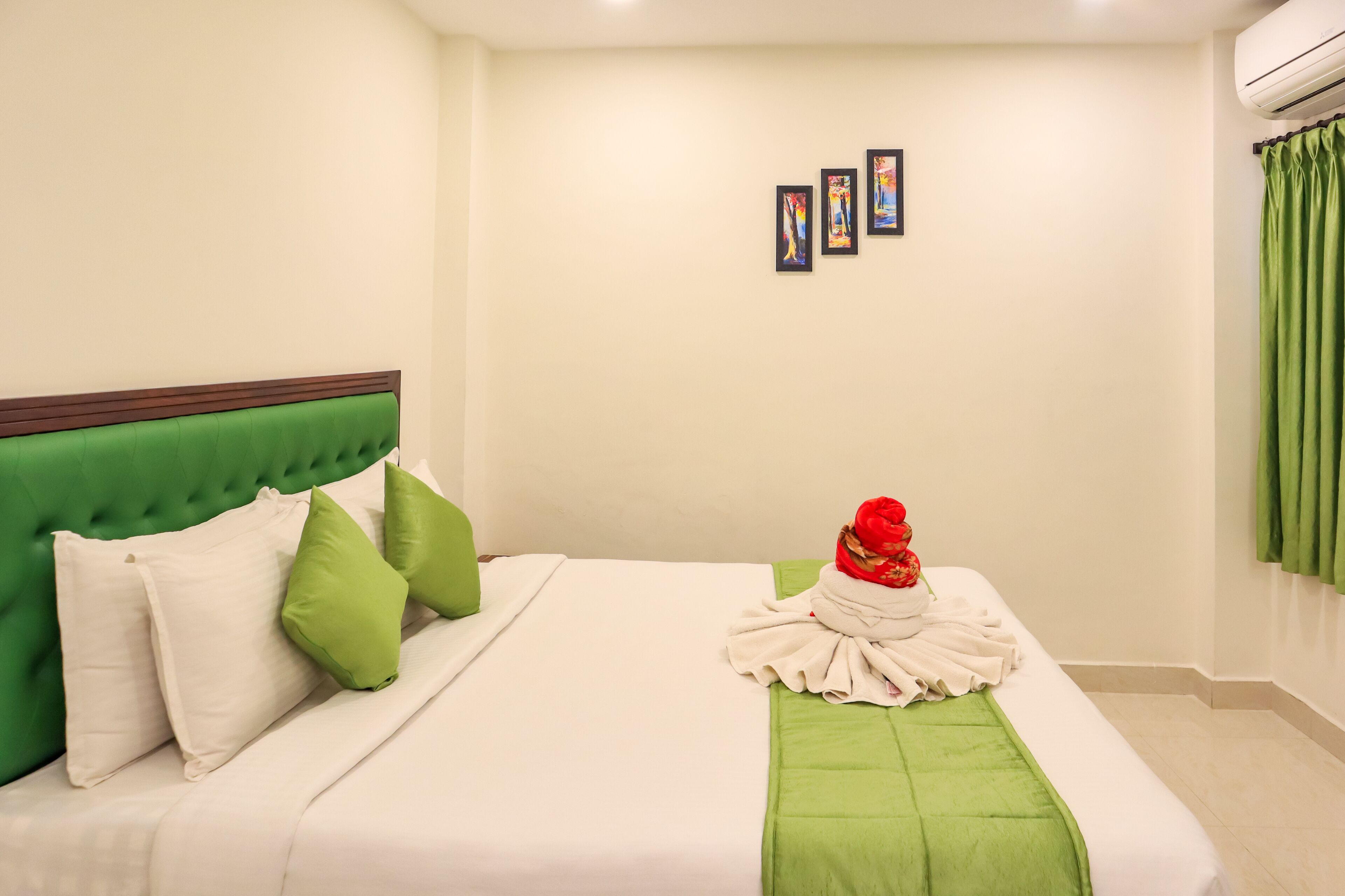 A hotel room with a green upholstered headboard, white bedding, and a green throw blanket.