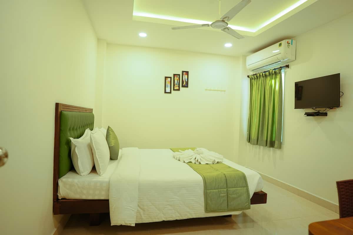 A hotel room with a bed, a ceiling fan, an air conditioning unit, a flat-screen TV, and a window with curtains.