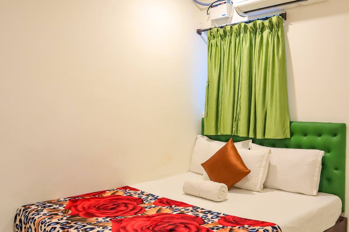 A bedroom with a bed, green curtains, a ceiling fan, and an air conditioning unit.