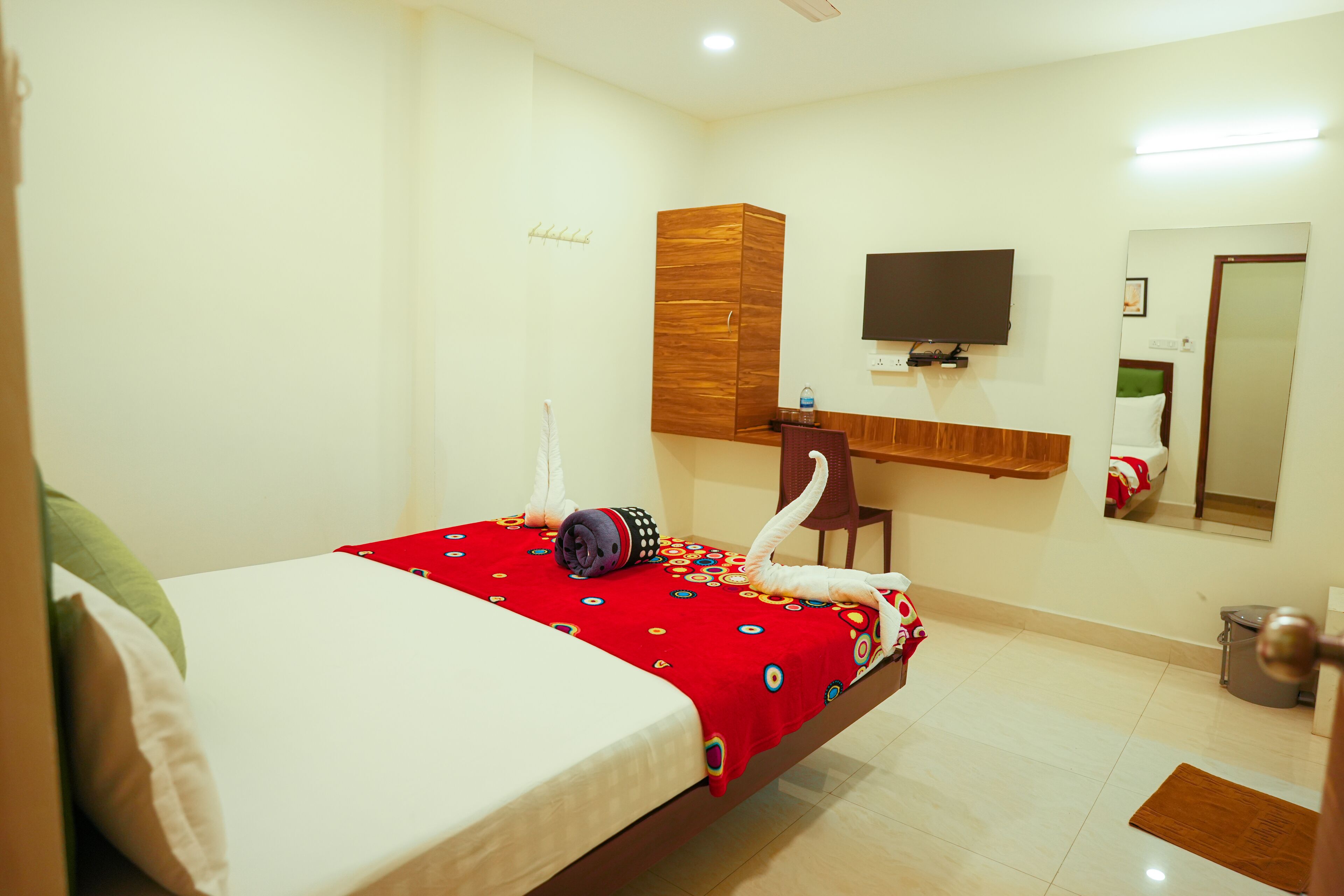 A hotel room with a bed, a wooden wardrobe, a television, and a mirror.