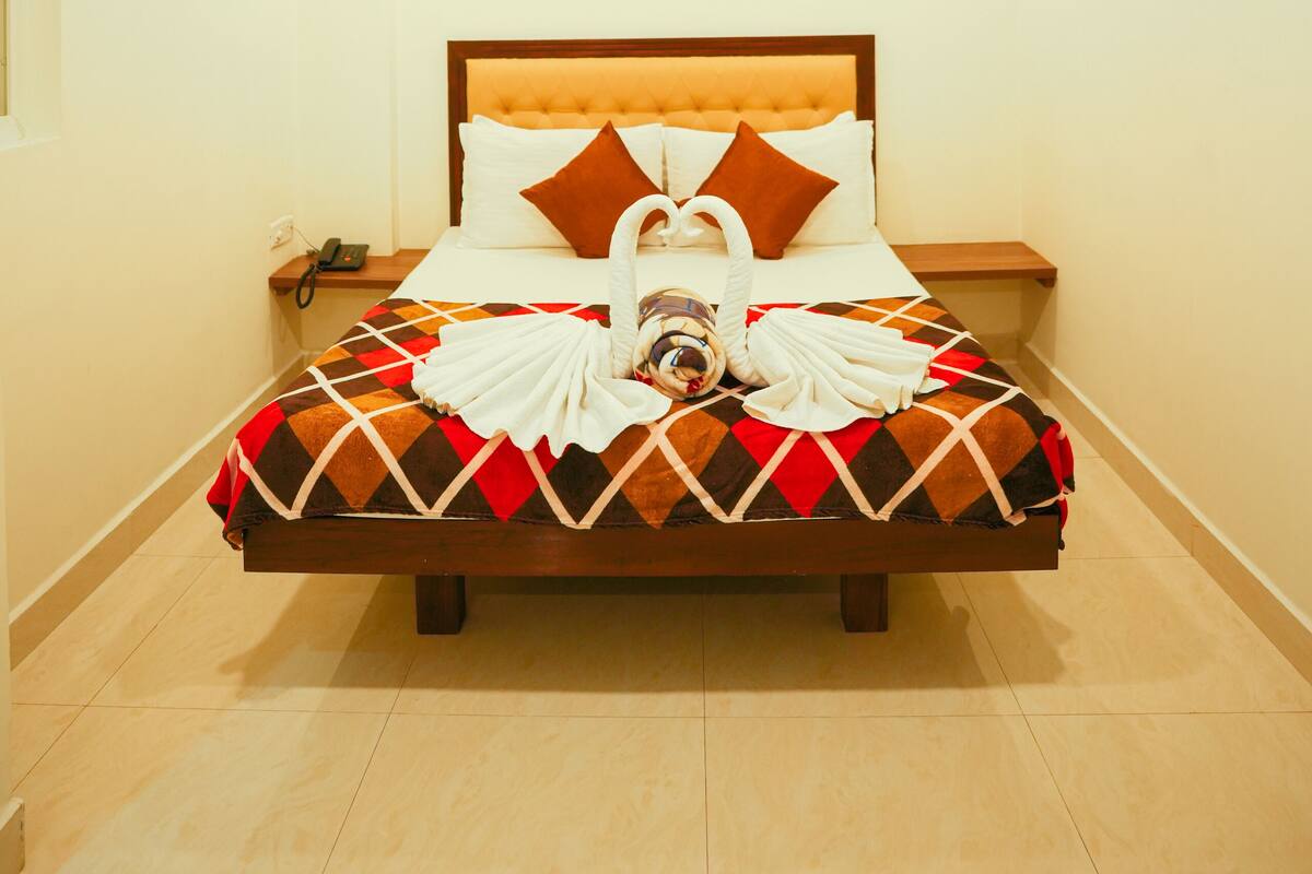 A neatly made bed with a patterned bedspread, a headboard, and a bedside table with a phone.