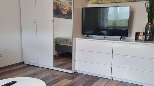 Moderni olohuone, jossa on televisio, valkoiset kaapit ja liukuovilla varustettu vaatekaappi.