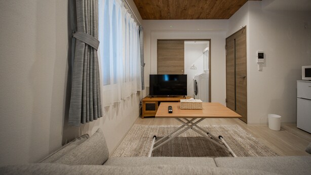 A modern living room with a wooden ceiling, a flat-screen TV, a wooden coffee table, and a sofa. - Astoria105 (Asahikawa)