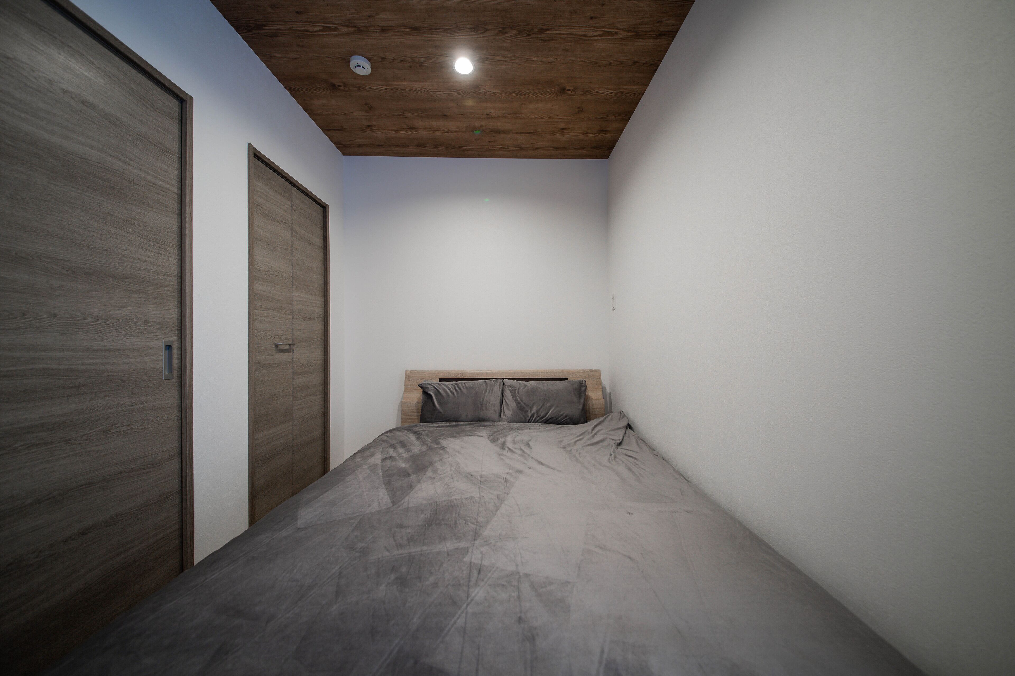 Un dormitorio con techo de madera, cama con ropa de cama gris y un armario de madera.