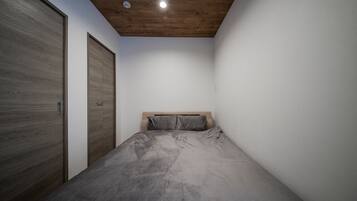 Un dormitorio con techo de madera, cama con ropa de cama gris y un armario de madera.