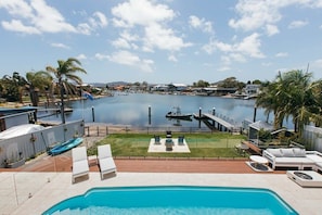 Een zwembadgedeelte met ligbedden, een klein terras en uitzicht op het water en omliggende huizen.