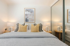 A hotel room with a bed, two bedside tables, a mirror, and a framed picture on the wall.