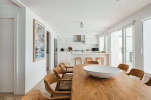 Een moderne keuken met witte kastjes, een centraal eiland en een eethoek met houten stoelen en een grote witte kom.