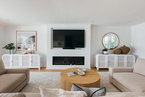Een woonkamer met een open haard, twee banken, een salontafel en een televisie.