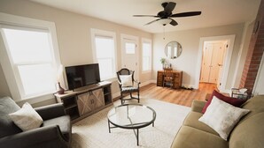 Un salon comprenant un canapé, un fauteuil, une table basse, un téléviseur et un ventilateur de plafond.