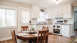 Une cuisine moderne avec des meubles blancs, un îlot central et un coin repas doté de chaises en bois.