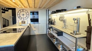 Una cocina moderna con vigas de madera en el techo, una isla central con estufa integrada y electrodomésticos de acero inoxidable.