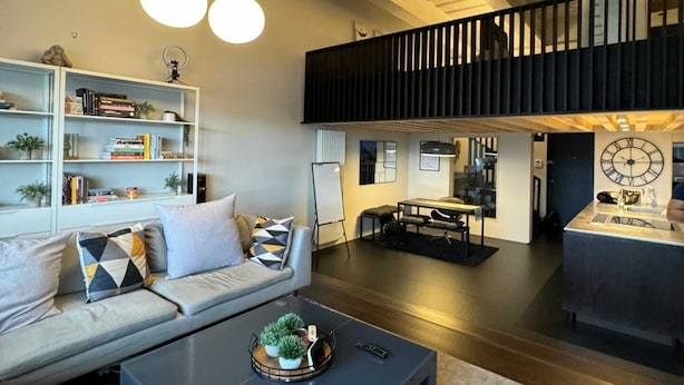 Amplio salón con diseño de estilo loft moderno, que incluye un techo alto, un nivel entre piso y una gran mesa de centro negra.