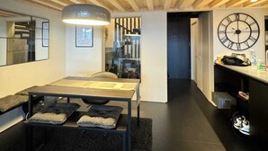 Un interior moderno con techo de madera, un área de comedor con mesa y bancos, una alfombra negra y un reloj de pared.