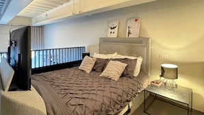 Un dormitorio moderno con una cama grande, televisor y una mesita de noche con lámpara.