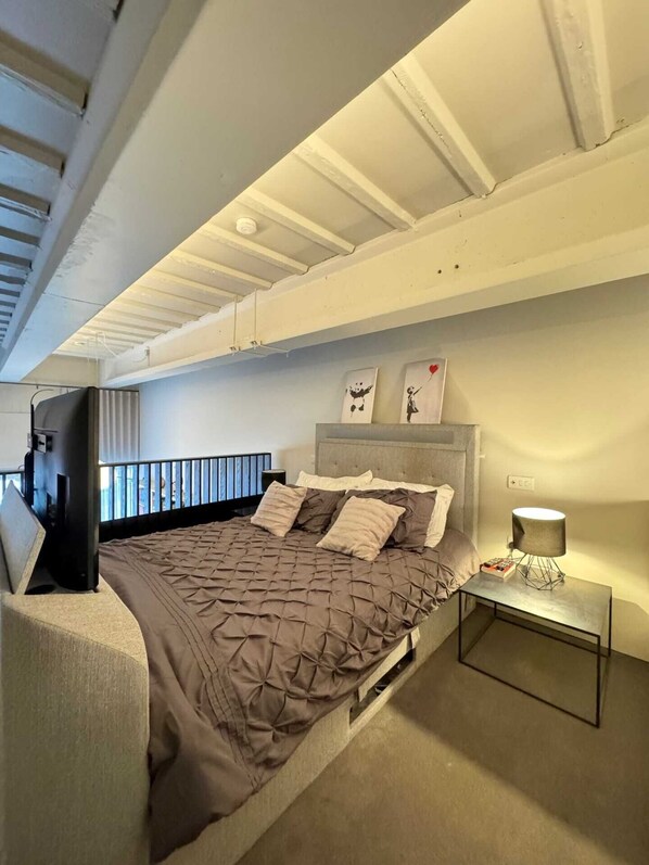 A modern bedroom with a large bed, a TV, and a bedside table with a lamp.
