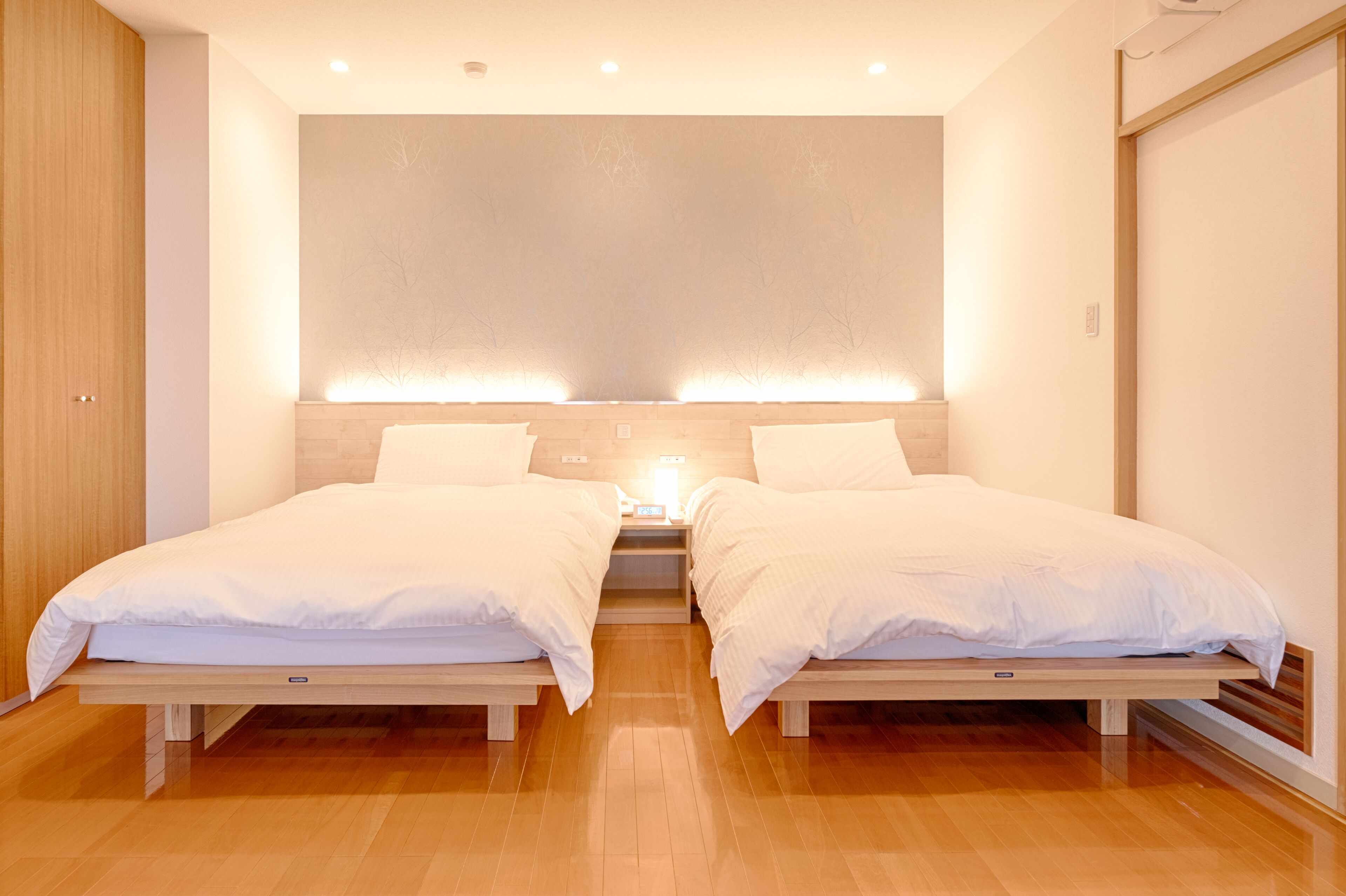 Una habitación de hotel moderna con dos camas individuales, suelo de madera y una paleta de colores neutros.