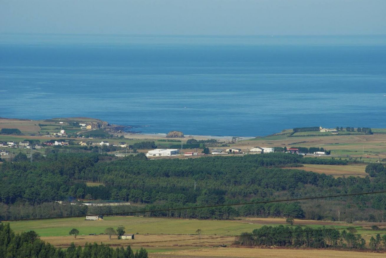Paisaje costero con edificios, campos y una masa de agua.