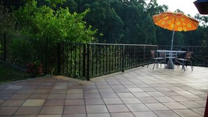 Un patio con suelo de baldosas, una cerca metálica y una mesa con sillas bajo una sombrilla.
