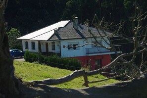 Une maison à deux étages, avec une façade rouge et blanche, une cheminée bien visible et un petit balcon.