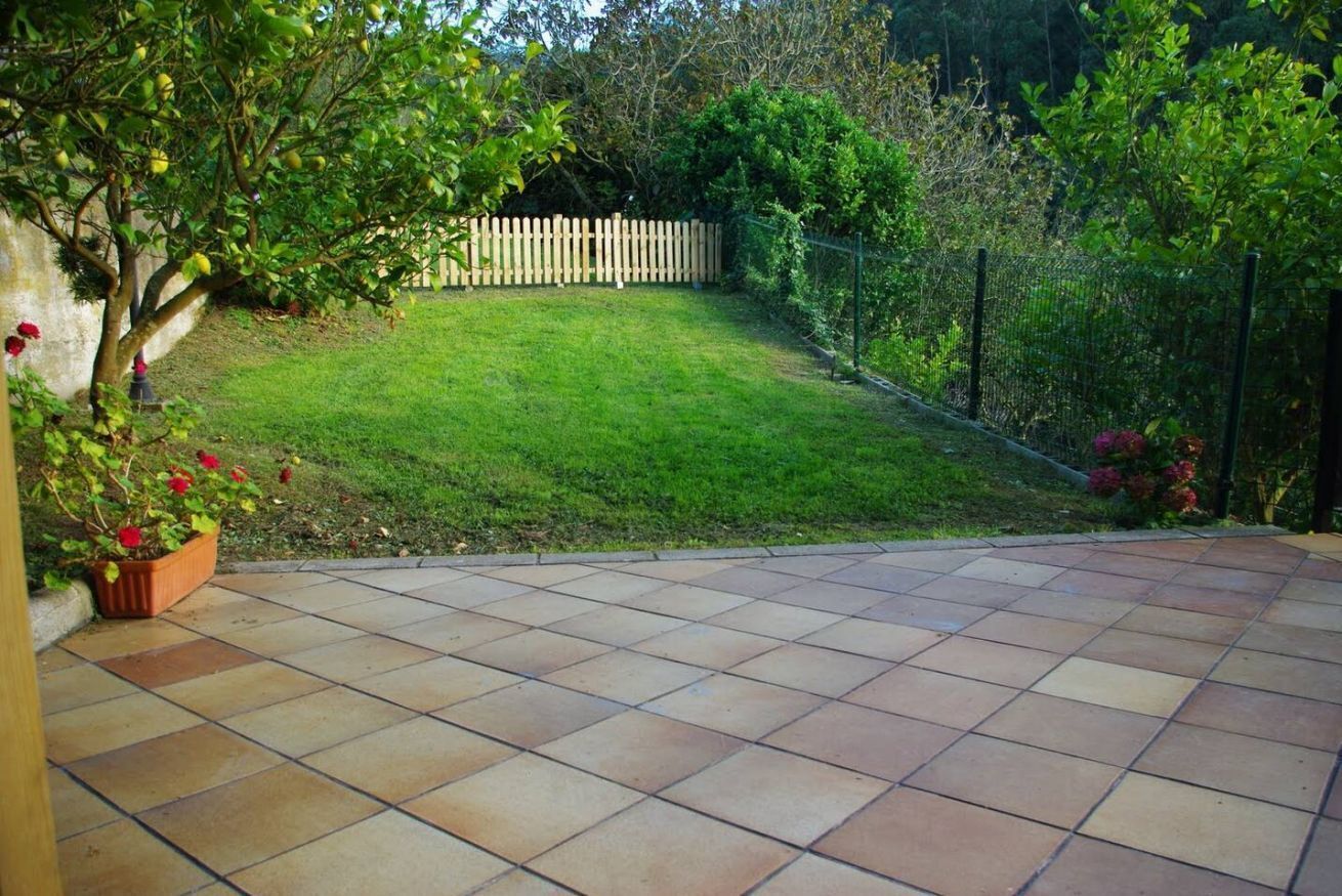 Un patio con piso de baldosas, cerca de madera y césped.
