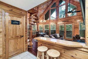 Interior de una cabaña de madera con una zona de bar, una escalera y un letrero que indica servicio de lavandería.