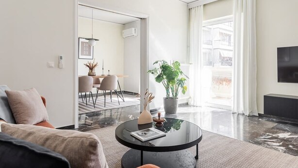 A modern living room with a round black coffee table, a sofa, and a dining area in the background. - Upscale 3BR Apartment in Chalandri (Chalandri)