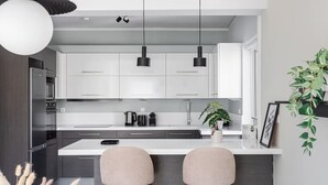A modern kitchen with white cabinets, two bar stools, a central island, and pendant lighting. - Upscale 3BR Apartment in Chalandri (Chalandri)