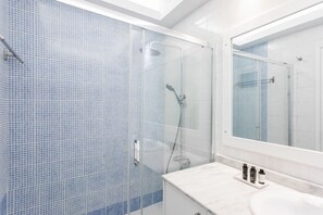 Un bagno moderno con doccia vetro, lavandino bianco e uno specchio grande.
