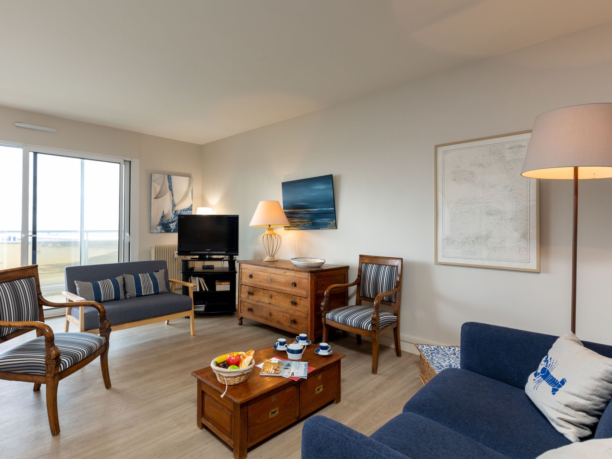 A modern living room with a sofa, chairs, a coffee table with fruit, a television, and artwork on the walls.