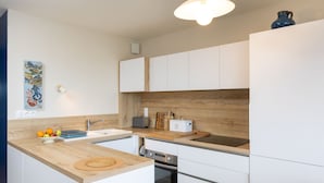 Eine moderne Küche mit weißen Schränken, einer Holzausziehtafel, einer Spüle, einem Toaster und einem kleinen Backofen.