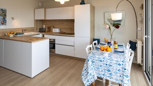 Eine moderne Küche mit Kochinsel, weißen Schränken und einem Essbereich mit Tisch für zwei Personen.