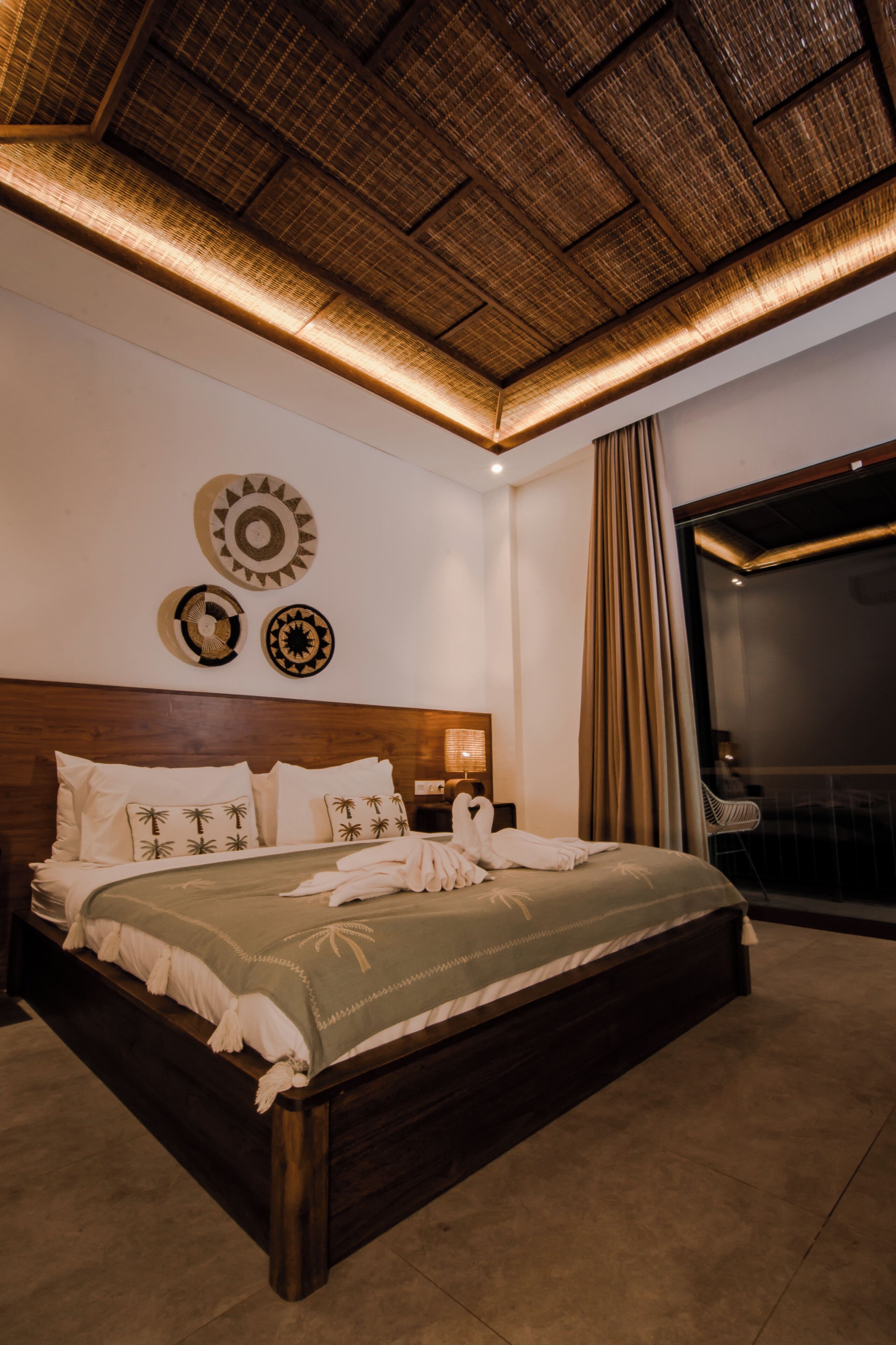 Une chambre d’hôtel avec un grand lit, une tête de lit en bois, un plafond orné d’un motif tissé et un balcon avec vue.