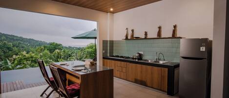 A modern kitchen with a wooden ceiling, a dining area with a view, and a green-tiled backsplash.