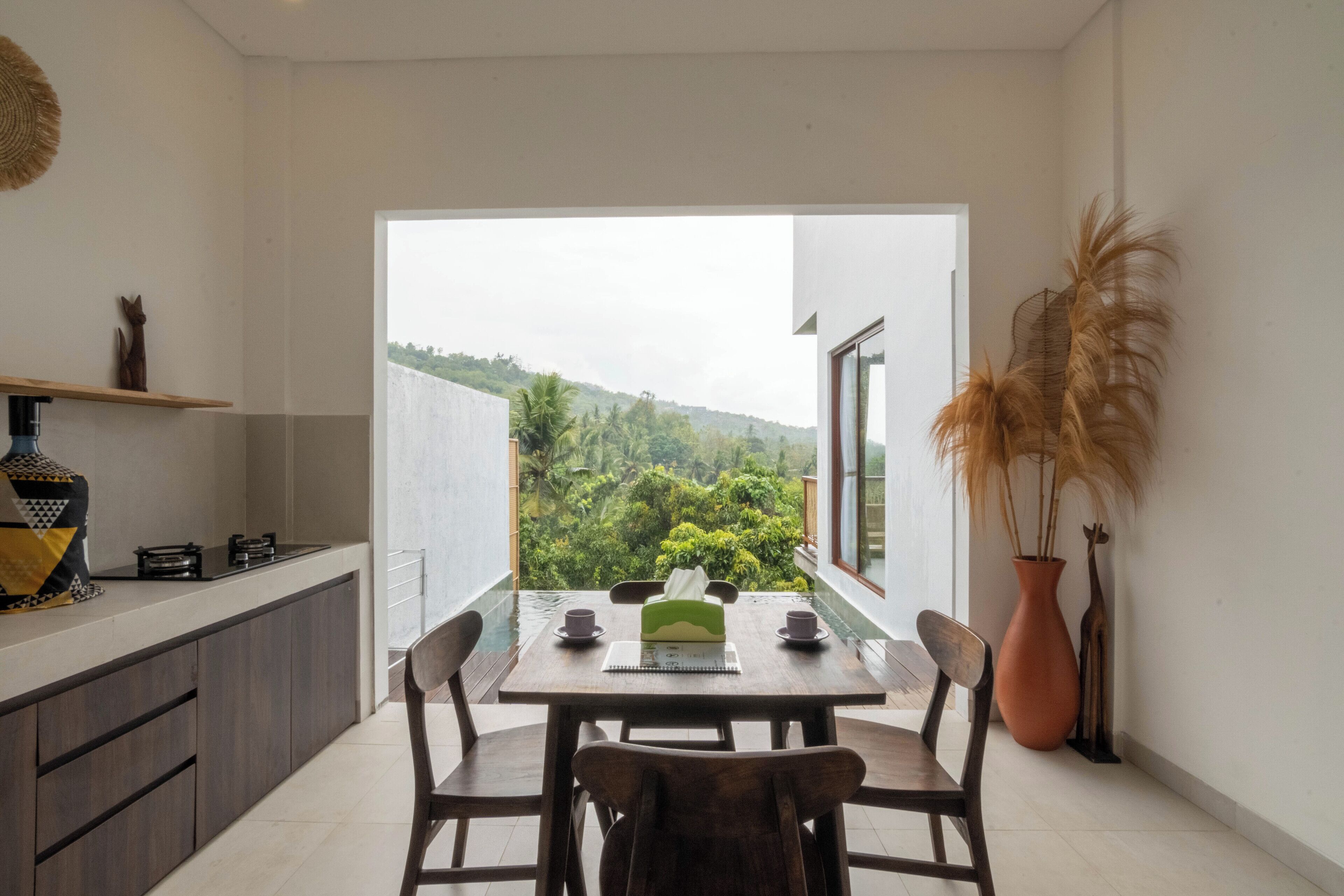 Un comedor con una mesa dispuesta para dos, una barra de cocina y vistas a un paisaje verde exuberante.
